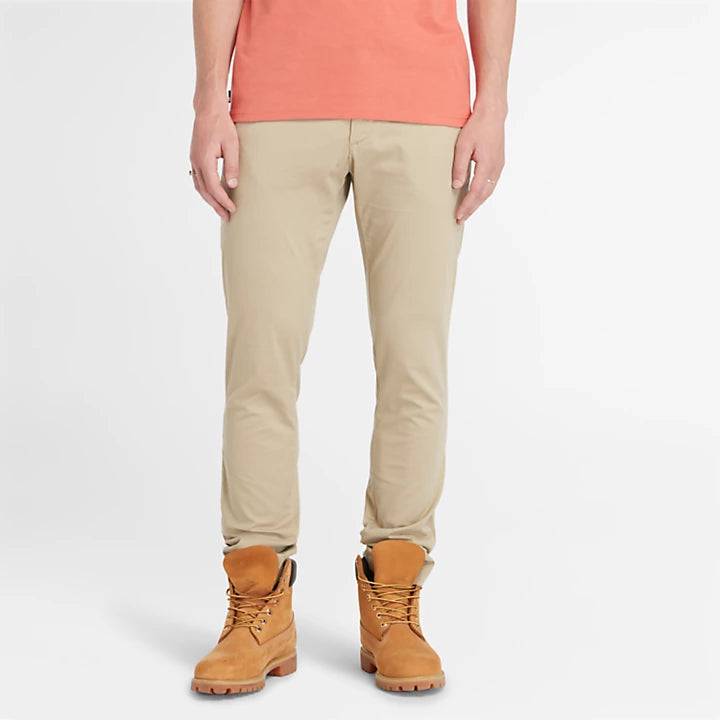 Timberland® Stretch Twill Chino Trousers for Men in Beige. Beige chino pants crafted from a blend of 97% organic cotton and 3% elastane (stretch) for comfort and freedom of movement. Features a classic chino design with belt loops, button fly closure, side pockets, and back pockets. Offers a relaxed fit for comfortable everyday wear.