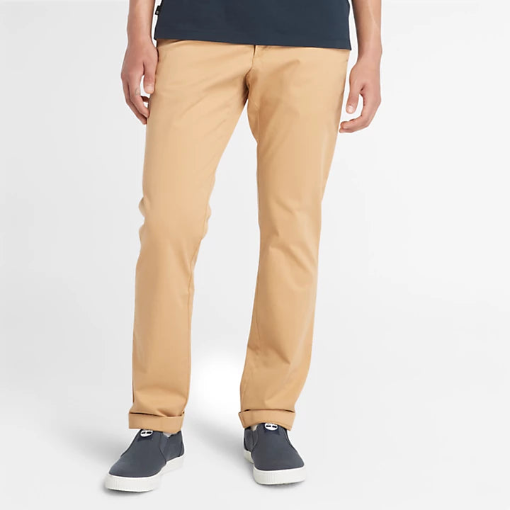 Light beige Timberland® Stretch Twill Chino Trousers for Men. Cotton blend fabric with stretch for comfort and mobility. Classic chino silhouette for timeless style. Flat front construction for a modern look. Belt loops for customized fit. Zip fly with button closure. Hand pockets for storage. Versatile light beige color. Pairs well with shirts, sweaters, or jackets.
