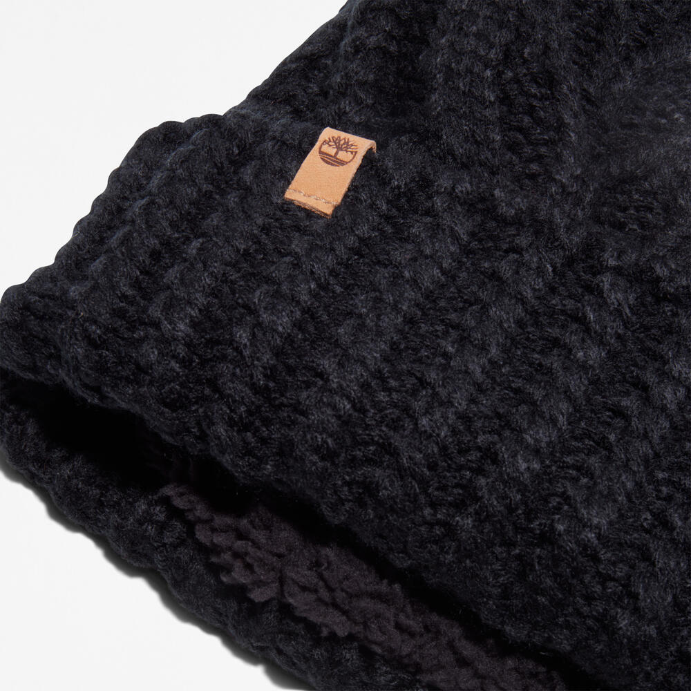 Black Timberland Cable Knit Pom Pom Beanie for Women. Soft and chunky cable knit for warmth and texture. Fold-over cuff for adjustability. Fluffy pom pom for a playful touch. Classic black color for versatility.