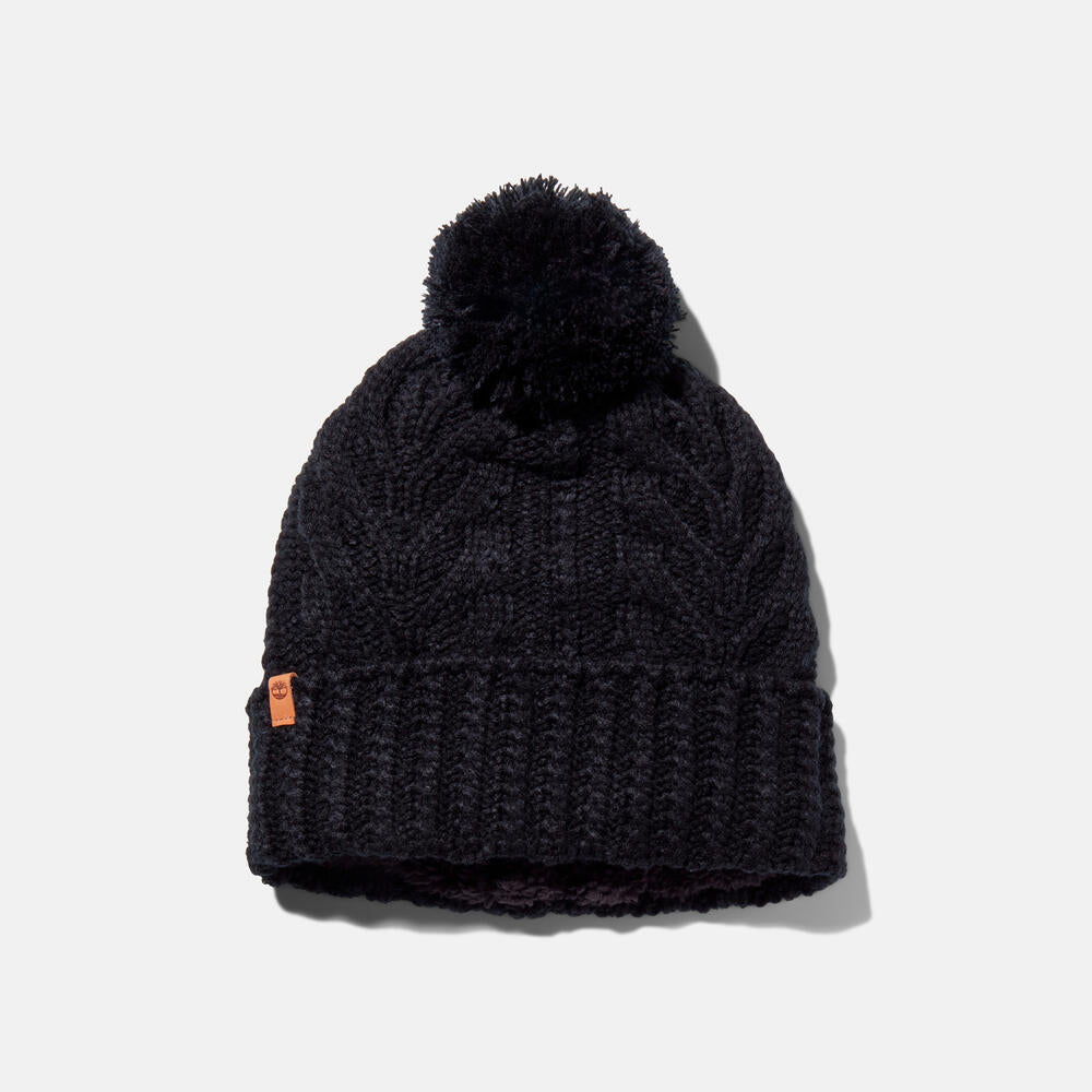 Black Timberland Cable Knit Pom Pom Beanie for Women. Soft and chunky cable knit for warmth and texture. Fold-over cuff for adjustability. Fluffy pom pom for a playful touch. Classic black color for versatility.