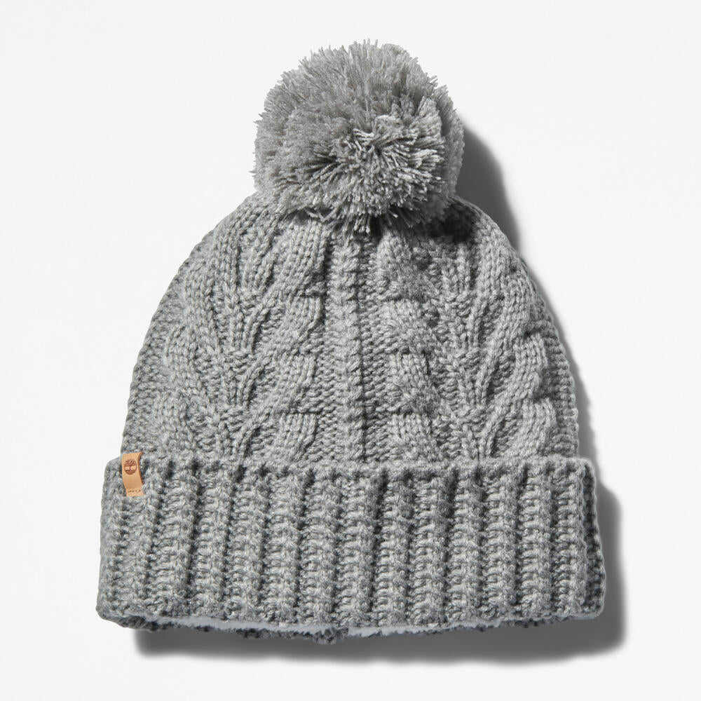 Grey Timberland® Cable Knit Pom Pom Beanie for Women. Soft and chunky cable knit for warmth and texture. Fold-over cuff for adjustability. Fluffy pom pom for a playful touch. Grey color for versatility.