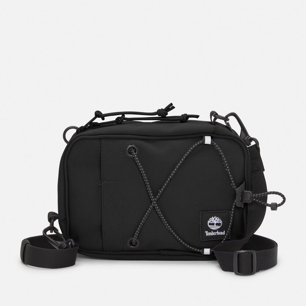 Timberland® Outdoor Archive 2.0 Crossbody Bag in Black. Black crossbody bag made from 100% recycled polyester. Features a large zipper opening, front panel slip pocket with bungee system, adjustable shoulder strap, and two ways to wear. Compact size and lightweight design. Sustainable choice for everyday use.