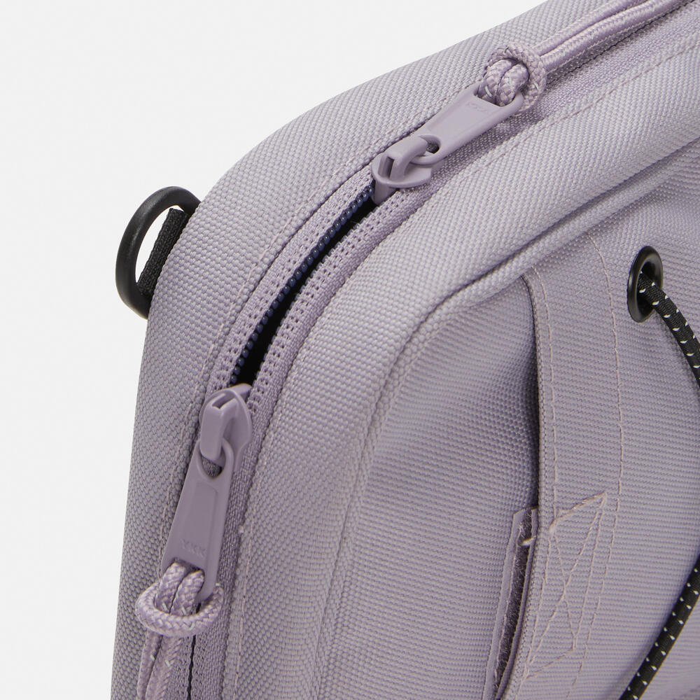 Timberland Outdoor Archive 2.0 Crossbody Bag in Lilac Ash. Lilac Ash crossbody bag made from 100% recycled polyester.Features a large zipper opening, front panel slip pocket with bungee system, adjustable shoulder strap, and two ways to wear. Compact size and lightweight design. Sustainable choice for everyday use.