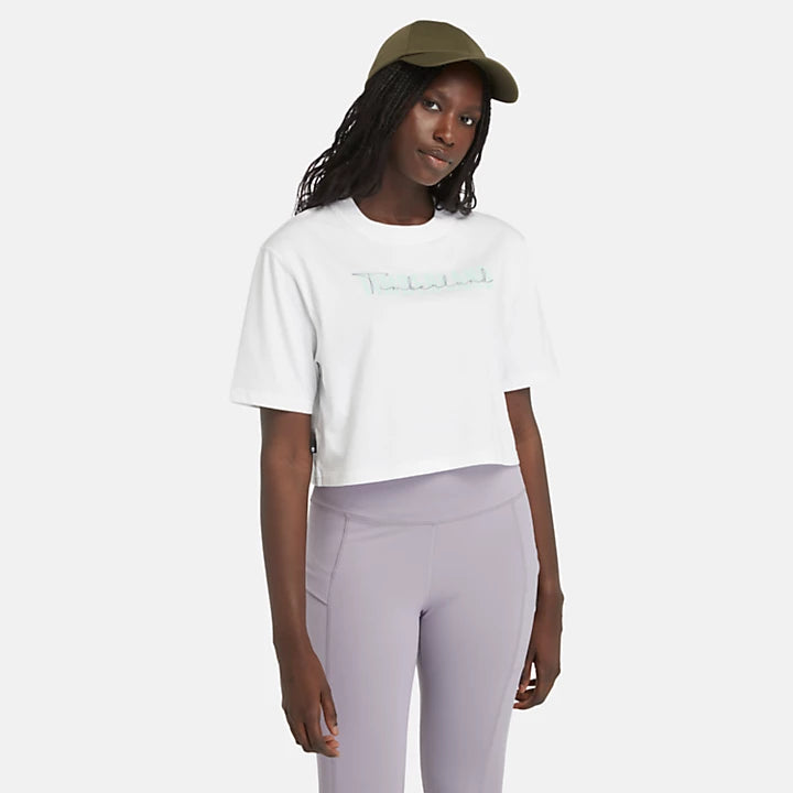 White Timberland® Cropped Short Sleeve Tee for Women. Soft, breathable 100% cotton. Relaxed fit for comfort. Cropped silhouette for a trendy look. Ribbed collar for a snug fit. Iridescent graphic print for eye-catching style