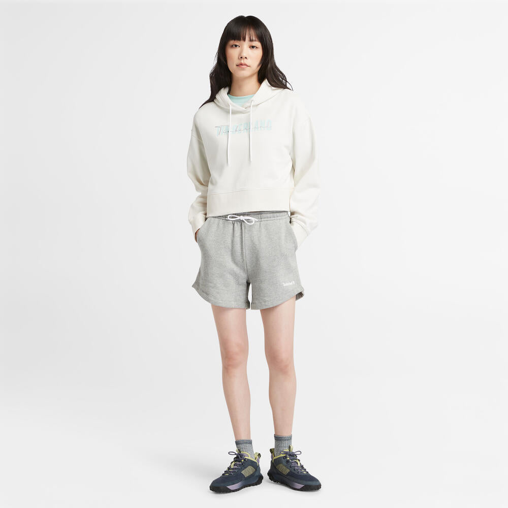 Vintage white Timberland Brushed Back Logo Hoodie for Women. Soft cotton-polyester blend for comfort. Brushed back fleece for warmth. Relaxed, cropped silhouette. Drawcord-adjustable hood. Iridescent Timberland logo