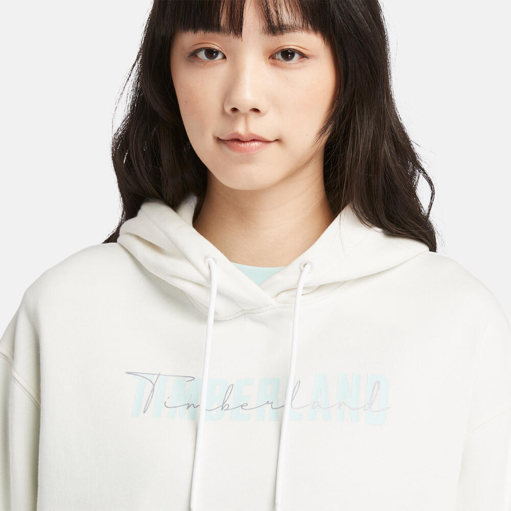 Vintage white Timberland Brushed Back Logo Hoodie for Women. Soft cotton-polyester blend for comfort. Brushed back fleece for warmth. Relaxed, cropped silhouette. Drawcord-adjustable hood. Iridescent Timberland logo