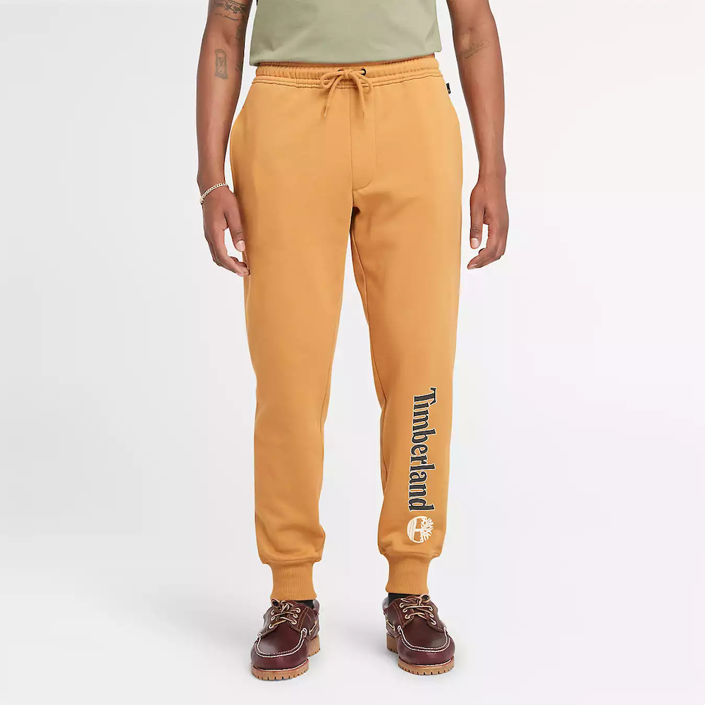 Wheat Timberland® Kennebec River Linear Logo Sweatpant for Men. Soft cotton blend fabric (85% cotton, 15% polyester) for comfort and breathability. Relaxed fit for comfortable wear. Elasticated drawcord waistband for customizable fit. Side pockets for storage.