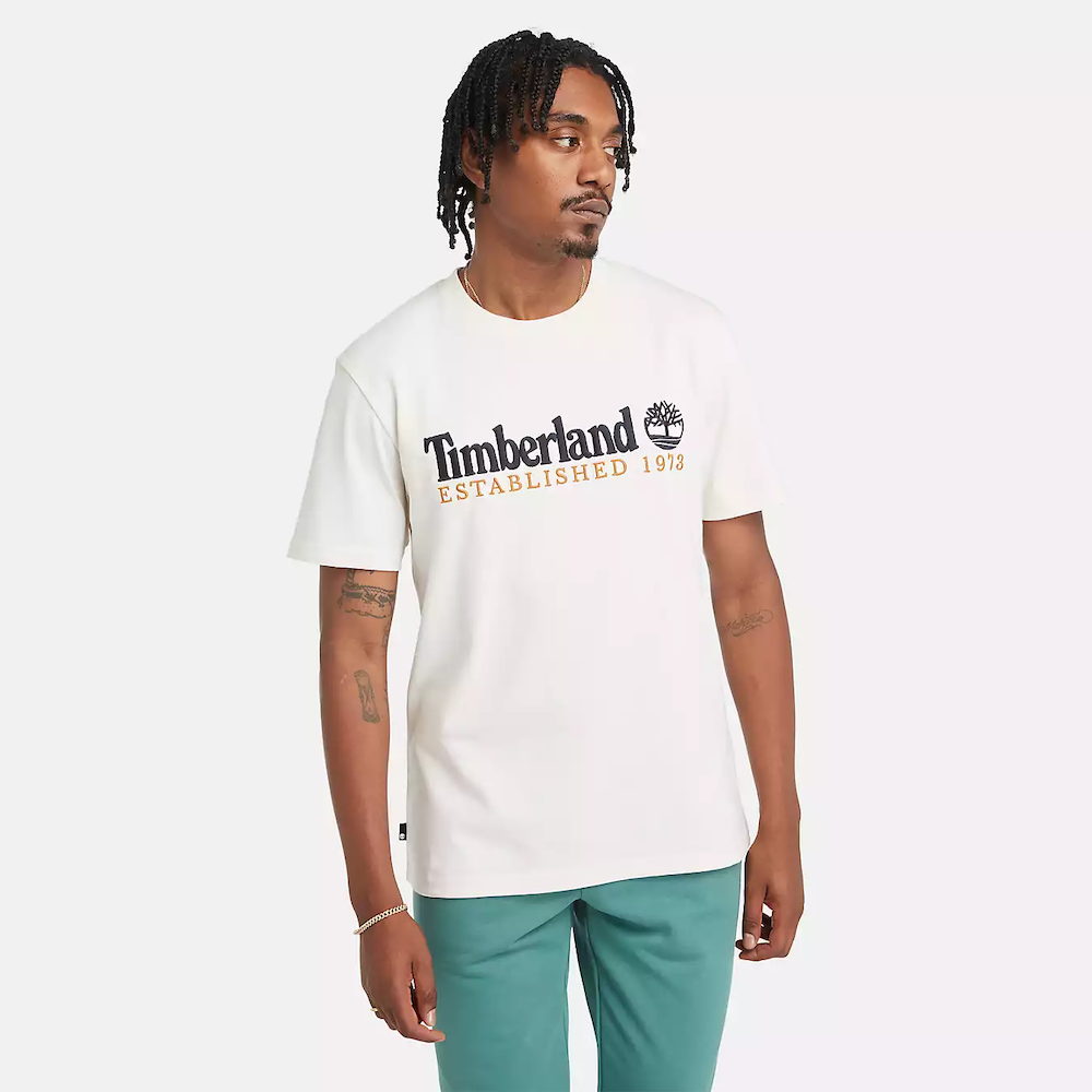 Vintage white Timberland® Kennebec River Linear Logo Tee. 100% cotton for softness and breathability. Crew neck, relaxed fit, short sleeves. Vintage white wash for a retro look. Logo print for heritage style. Pairs well with casual pants.